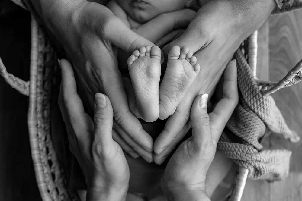 Pieds de nouveau-né tenus dans les mains des parents, en noir et blanc.