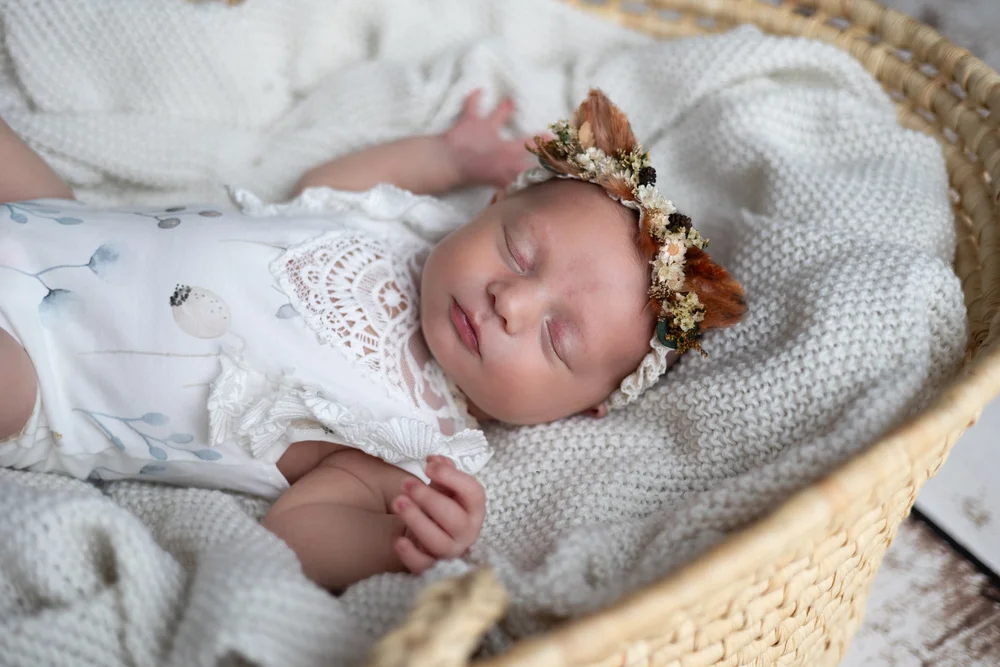 Nouveau-né en tenue de dentelle blanche, couronne de fleurs, dans un panier.