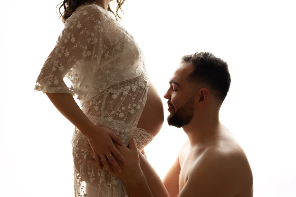 Homme embrassant le ventre de sa compagne en robe de dentelle.