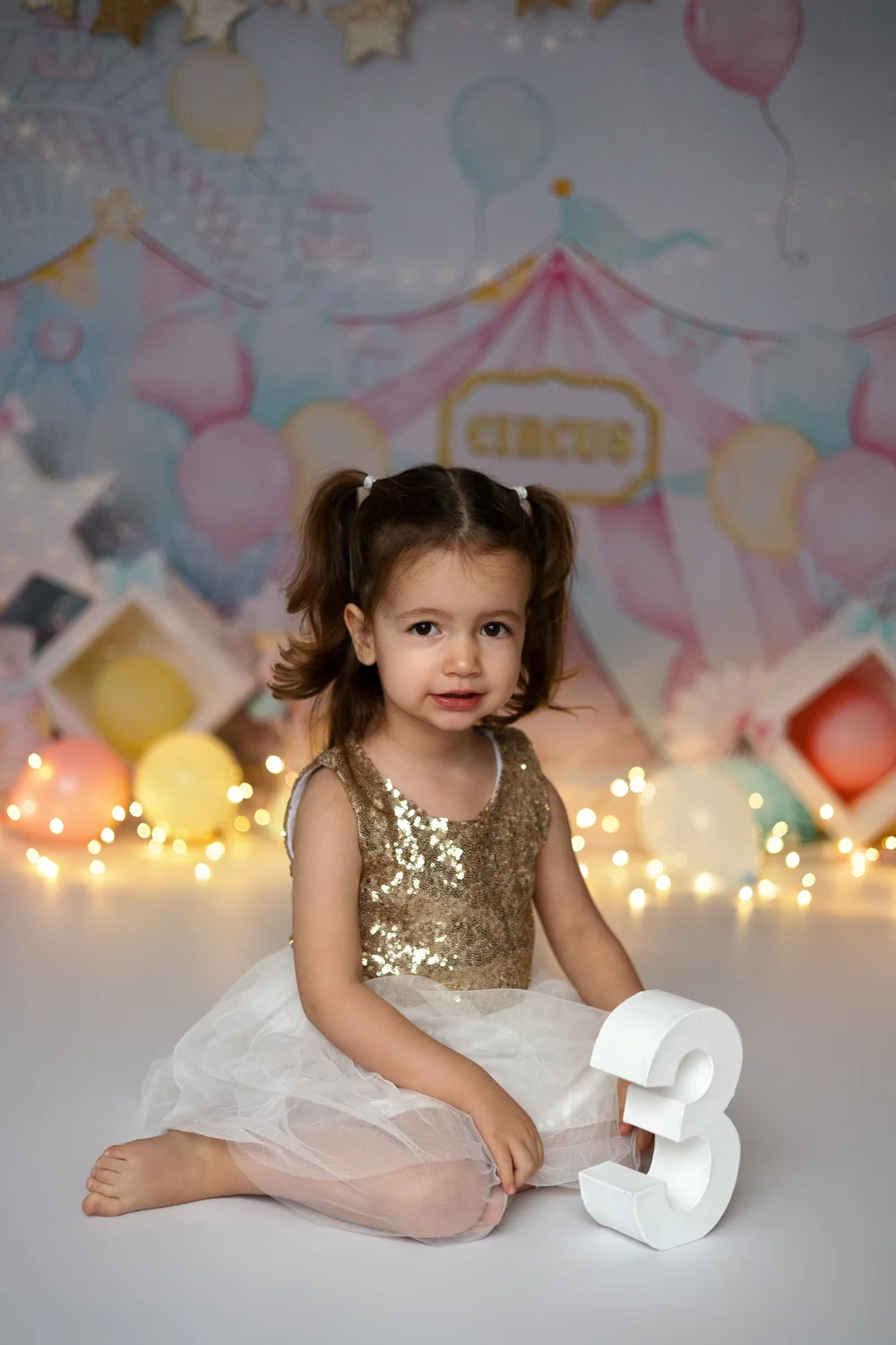 Petite fille en robe dorée devant un décor de cirque, avec un chiffre 3.