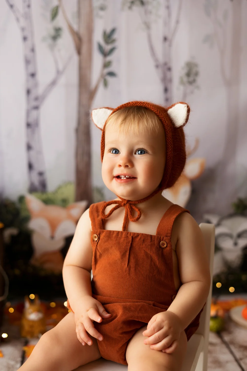 Bébé en costume de renard assis devant un décor de forêt.