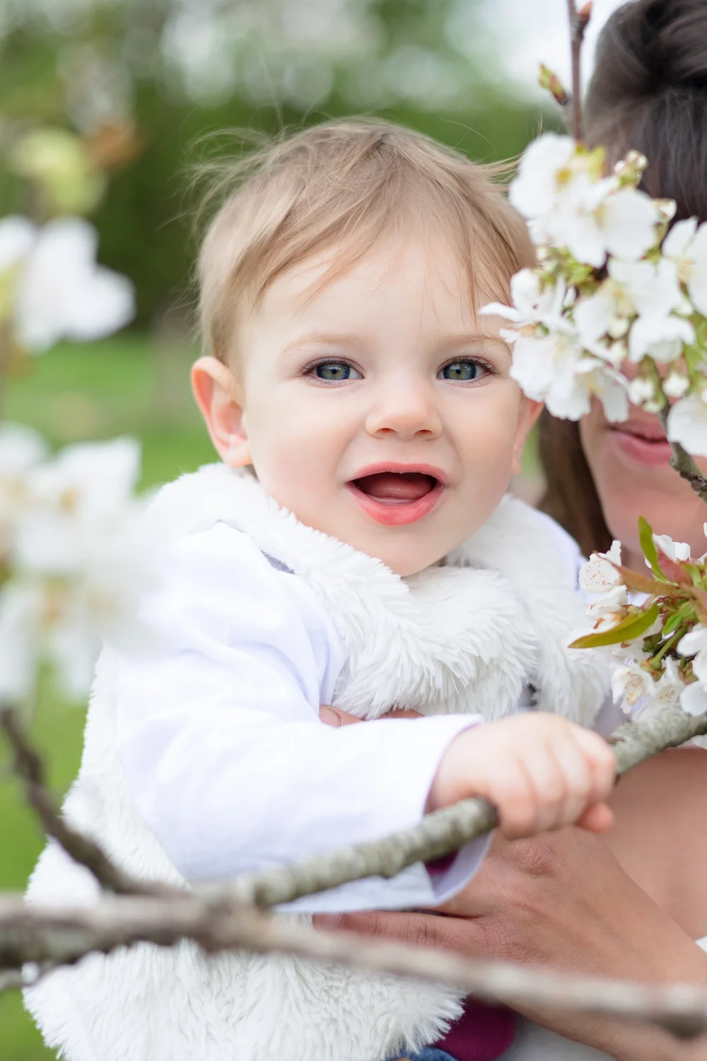 Bébé souriant dans les bras de sa maman, sous un arbre en fleurs.
