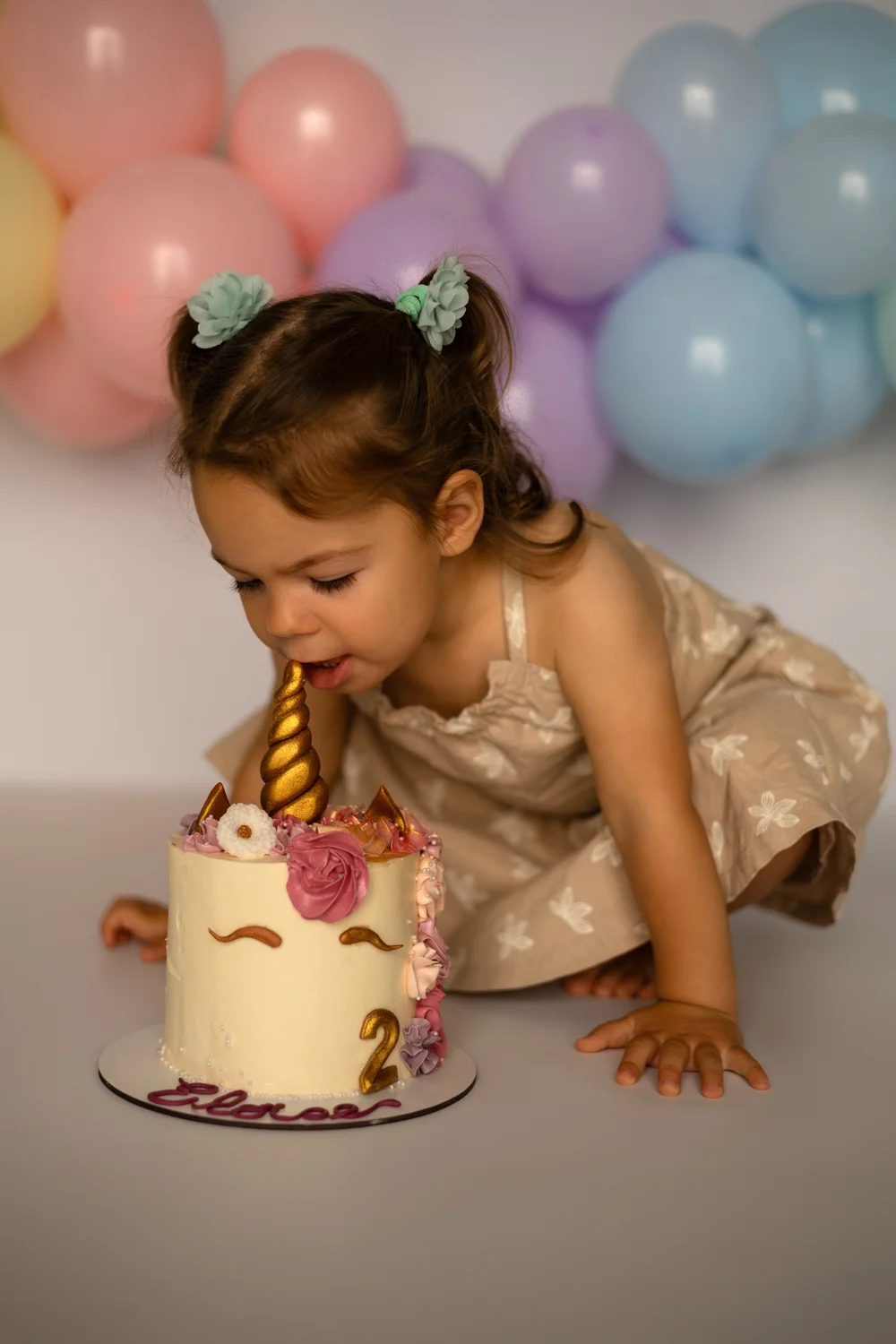 Petite fille goûtant son gâteau licorne devant des ballons pastel.