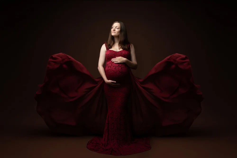 Femme enceinte en robe rouge drapée, en studio sur fond brun.