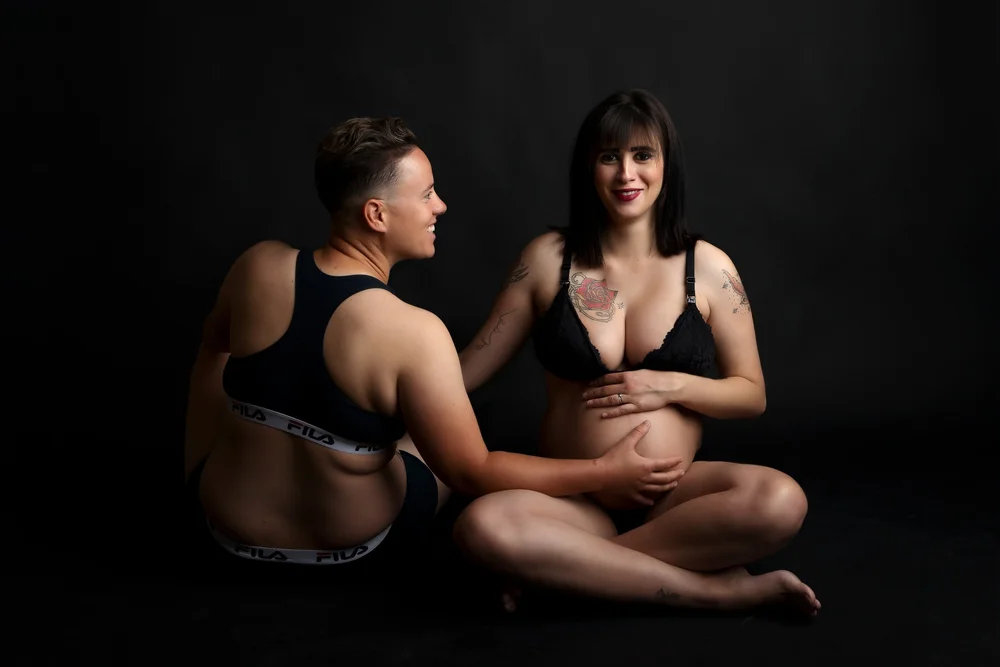 Couple en studio sur fond noir, main sur le ventre.