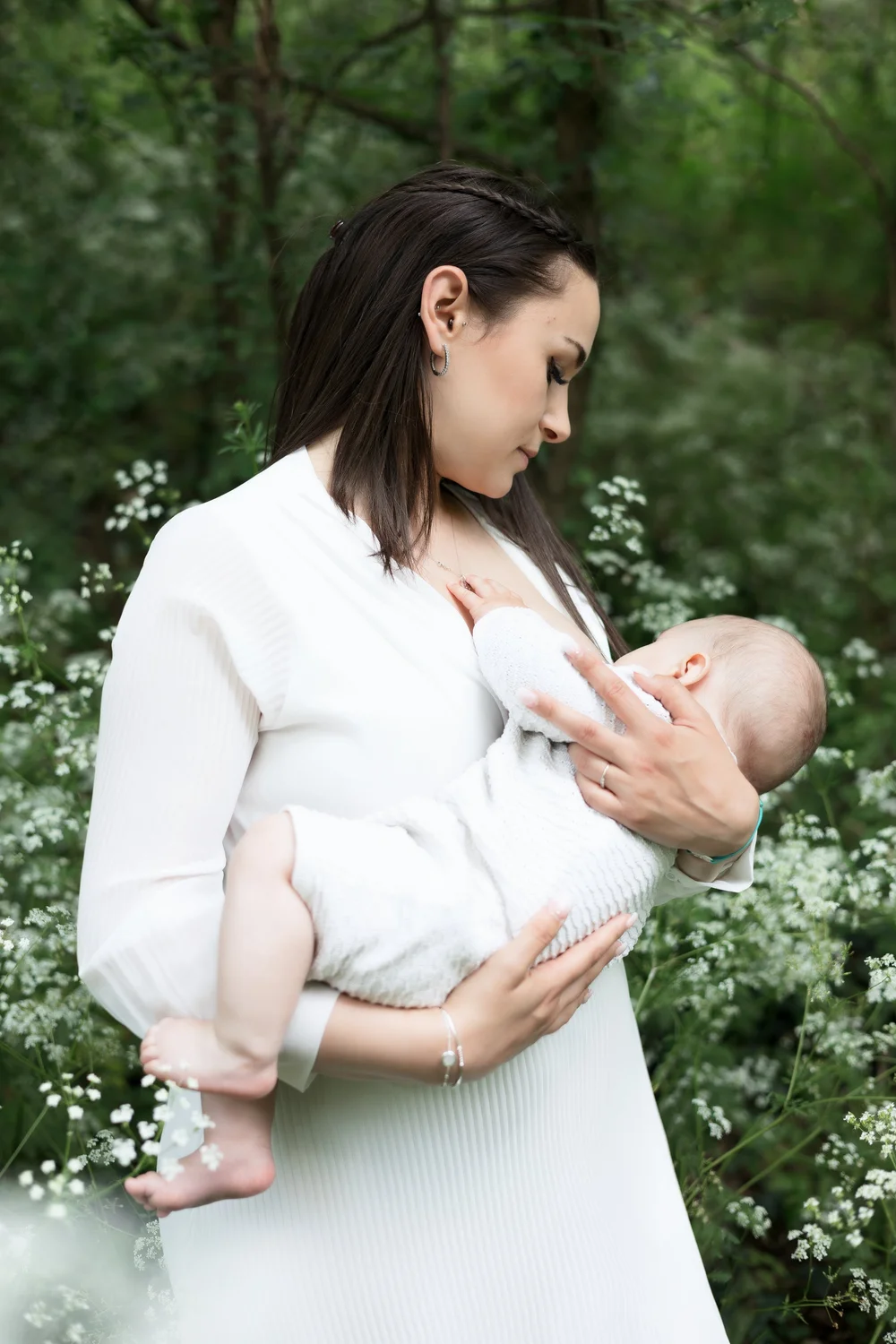 Maman en robe blanche allaitant son bébé dans la nature.