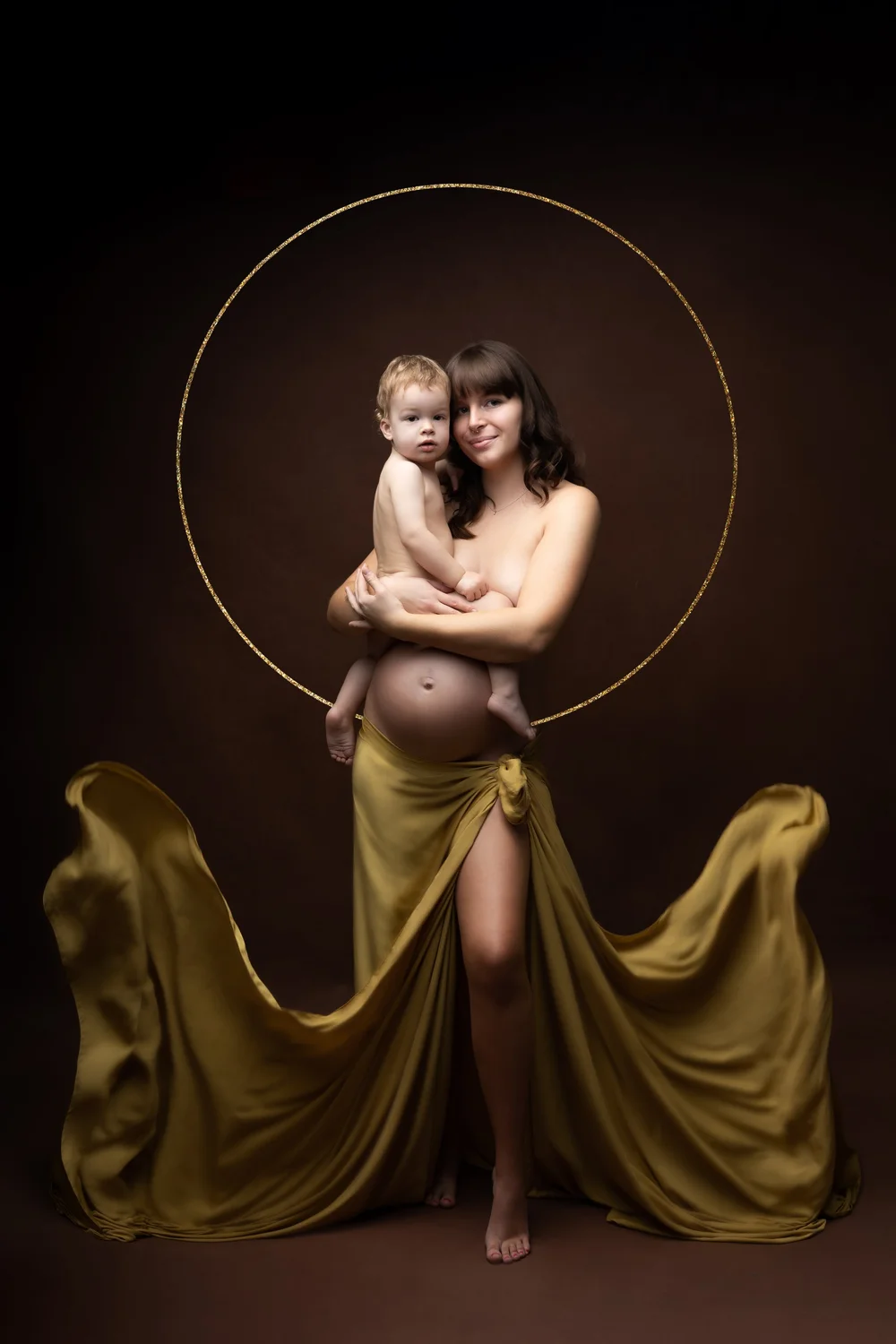 Maman enceinte portant son enfant sous un cercle doré, drapée d’or.