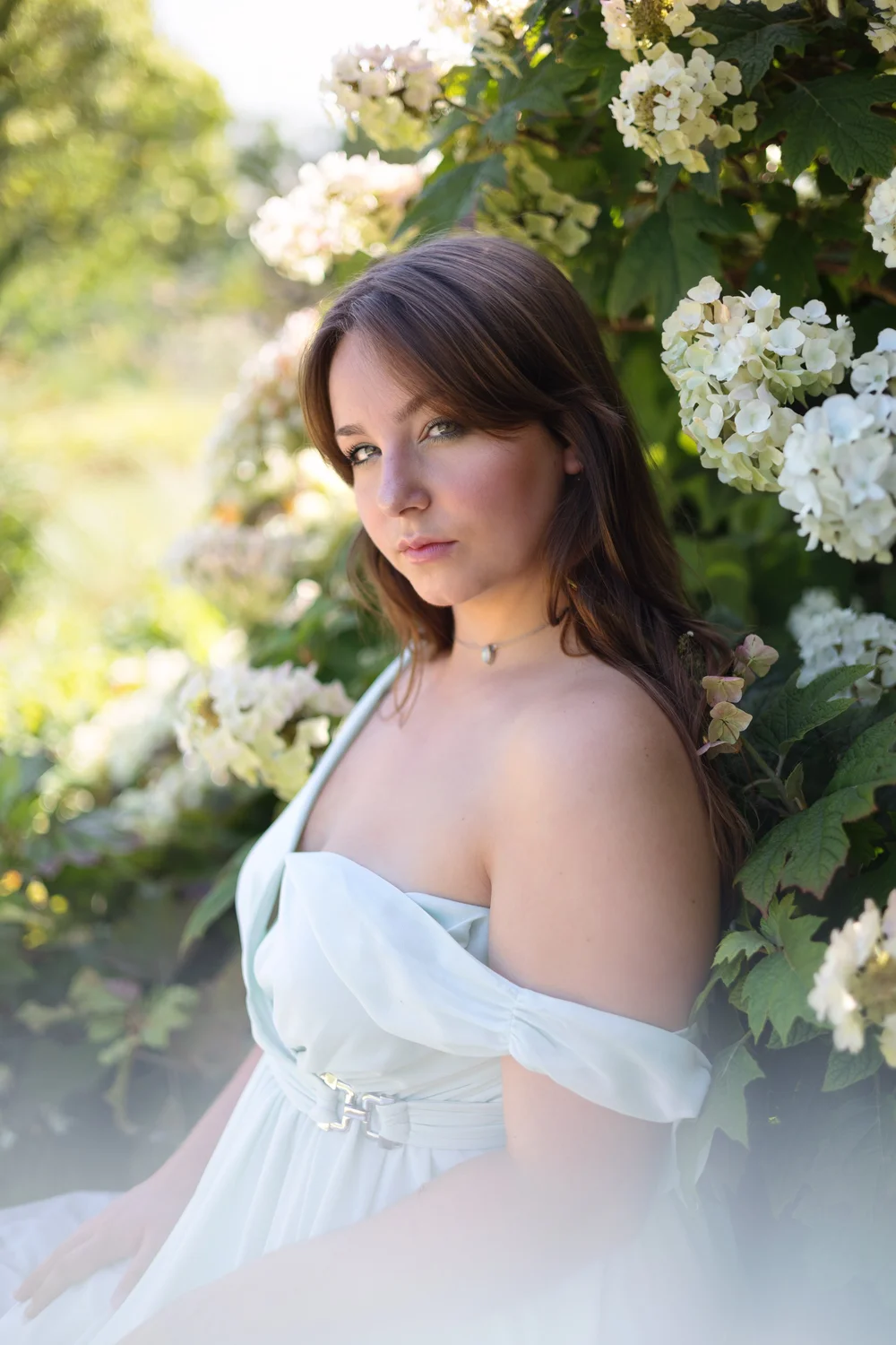 Femme en robe blanche devant un rosier blanc.