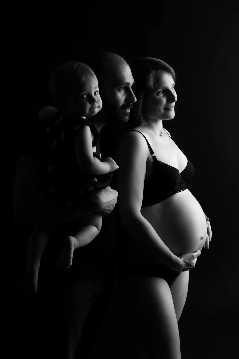 Famille en clair-obscur avec un bébé, sur fond noir.
