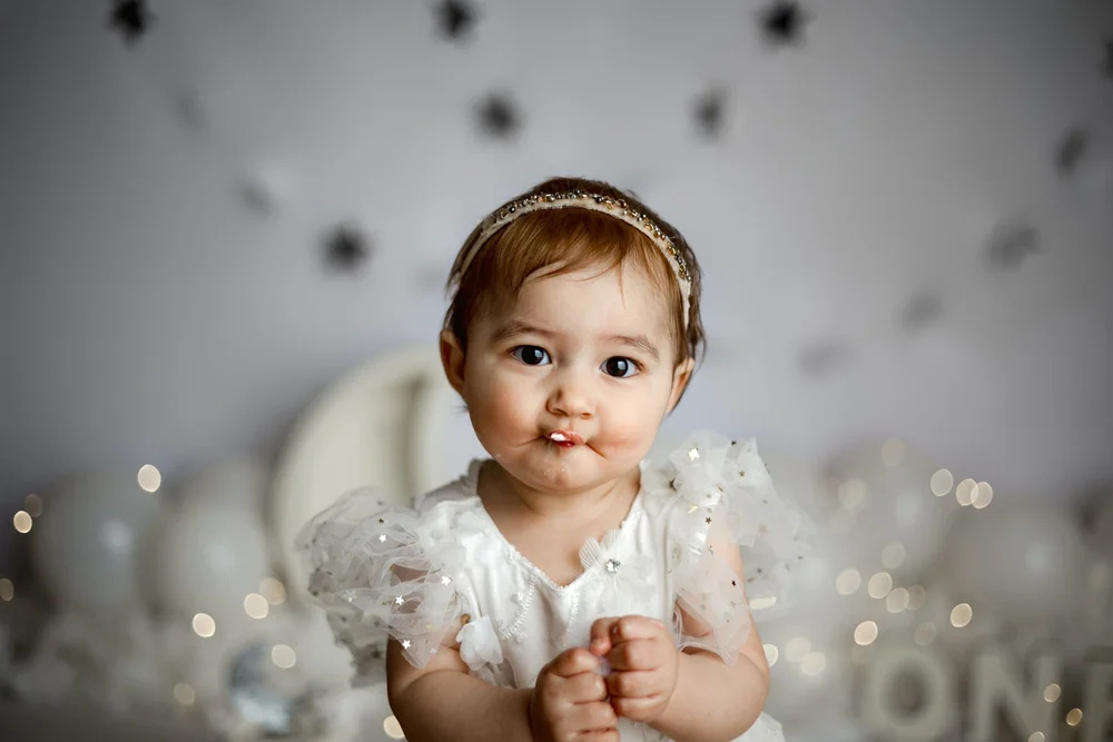 Bébé en robe blanche devant un décor de nuages et d’étoiles.
