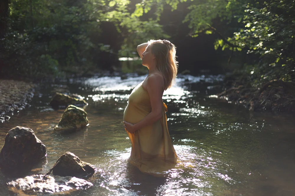 Femme enceinte dans une rivière au soleil, en forêt.