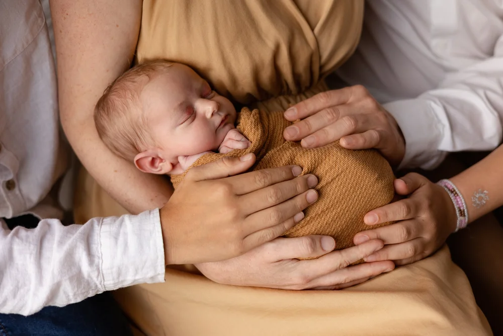 Nouveau-né en tenue moutarde dans les bras de ses parents.