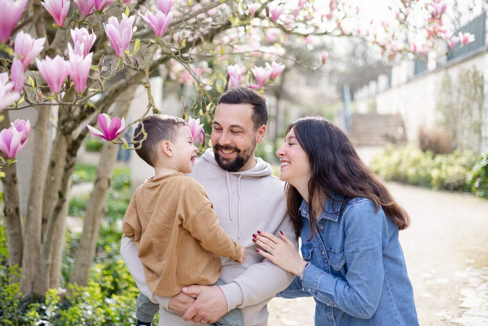Parents riant avec leur petit garçon sous un magnolia en fleurs.