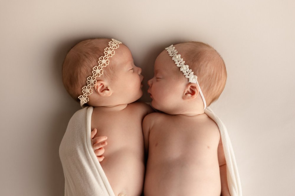 Jumeaux nouveau-nés endormis côte à côte, avec des bandeaux fleuris.
