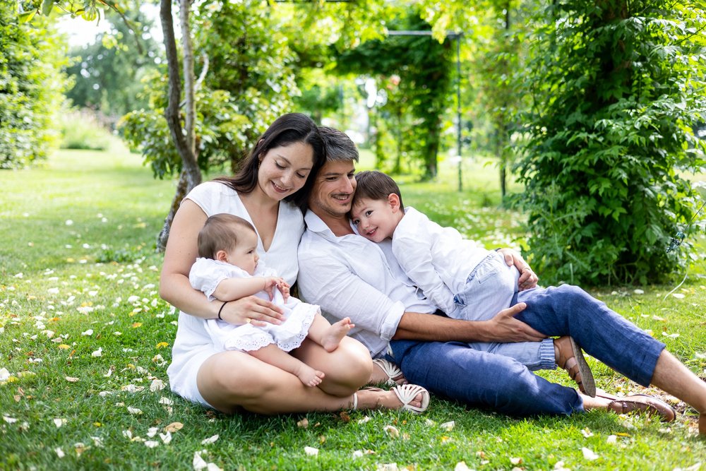 Parents et leurs deux enfants allongés dans l’herbe d’un parc, sous les arbres.