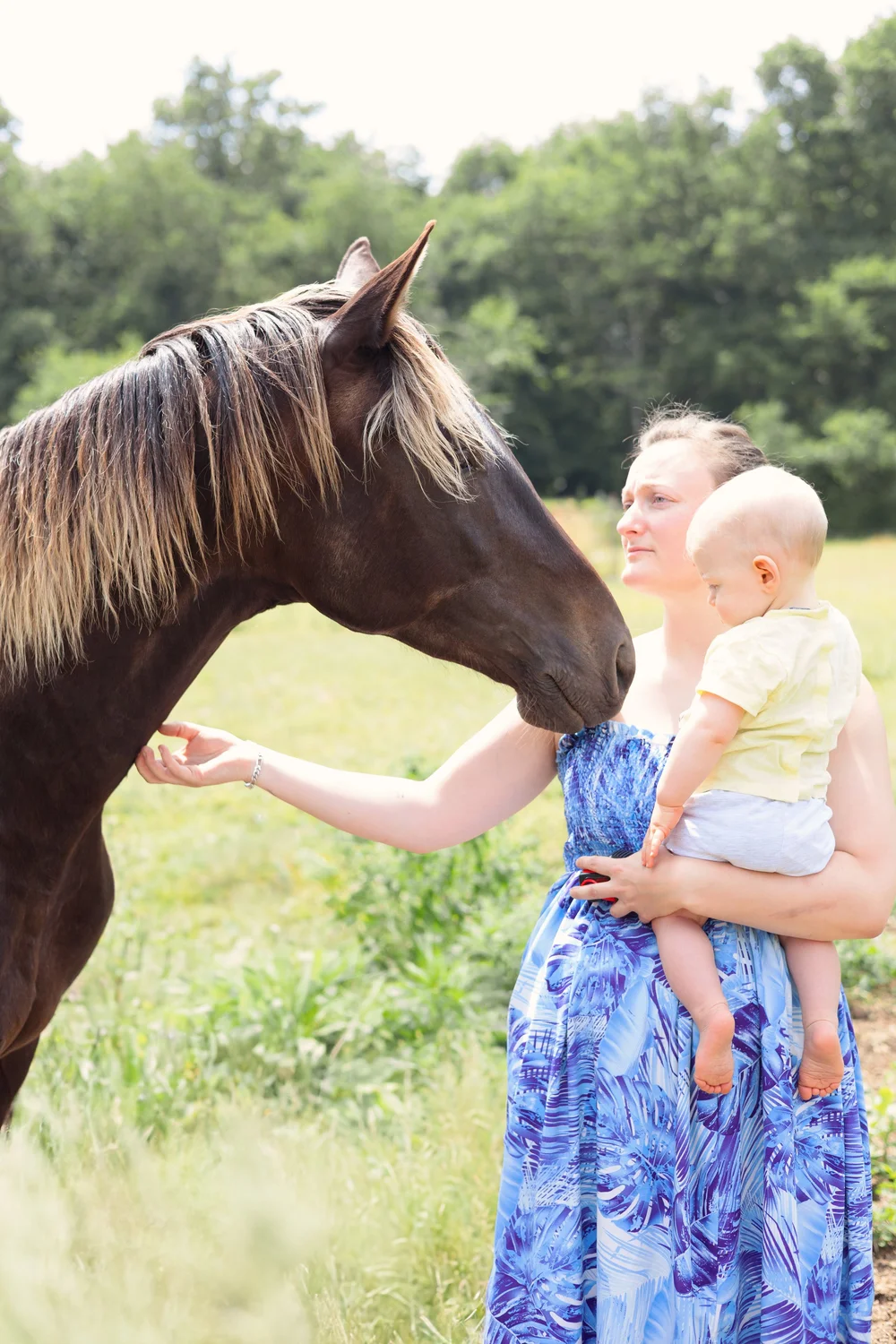 Maman en robe bleue avec son bébé caressant un cheval.