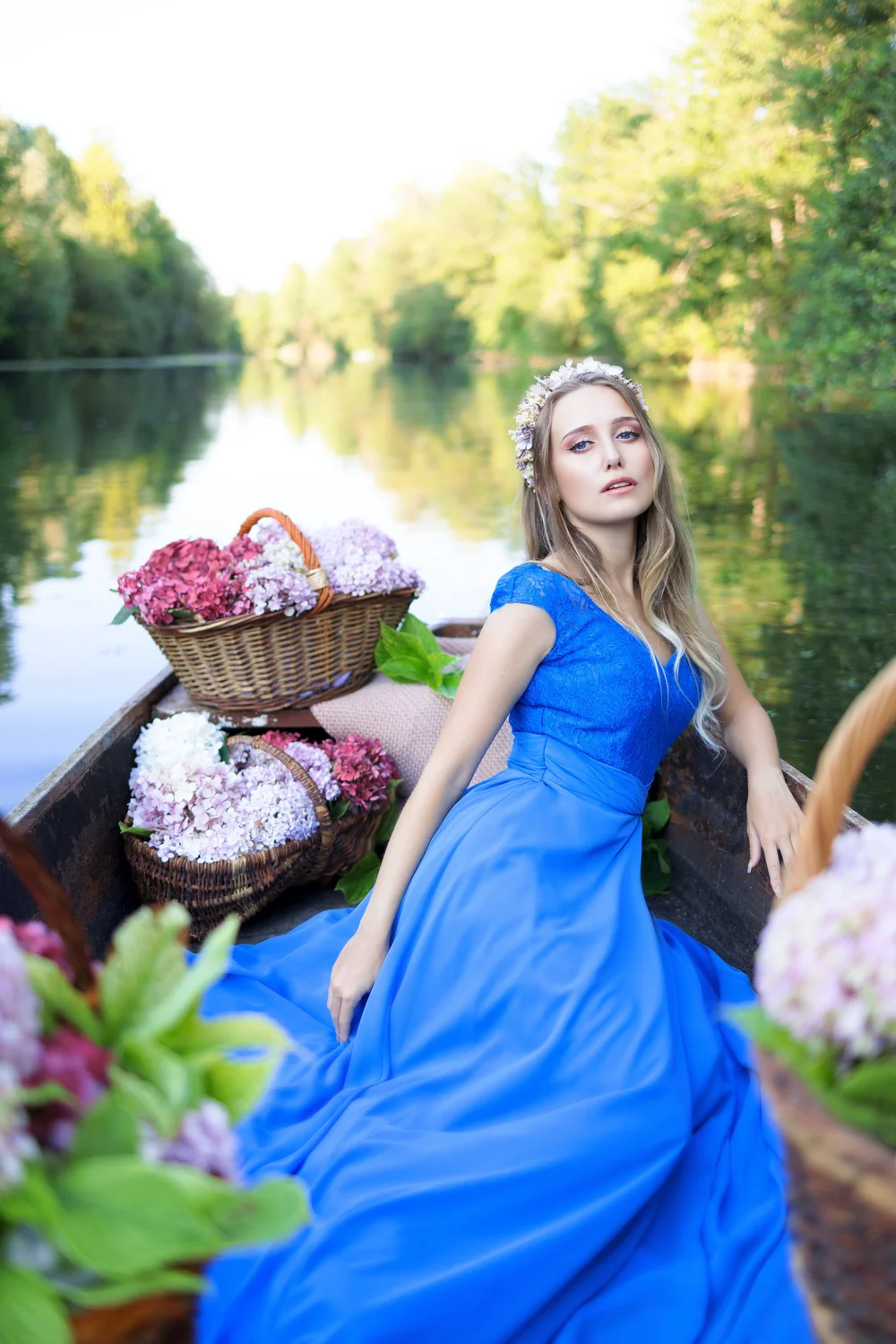 Femme en robe bleue dans une barque fleurie sur une rivière.