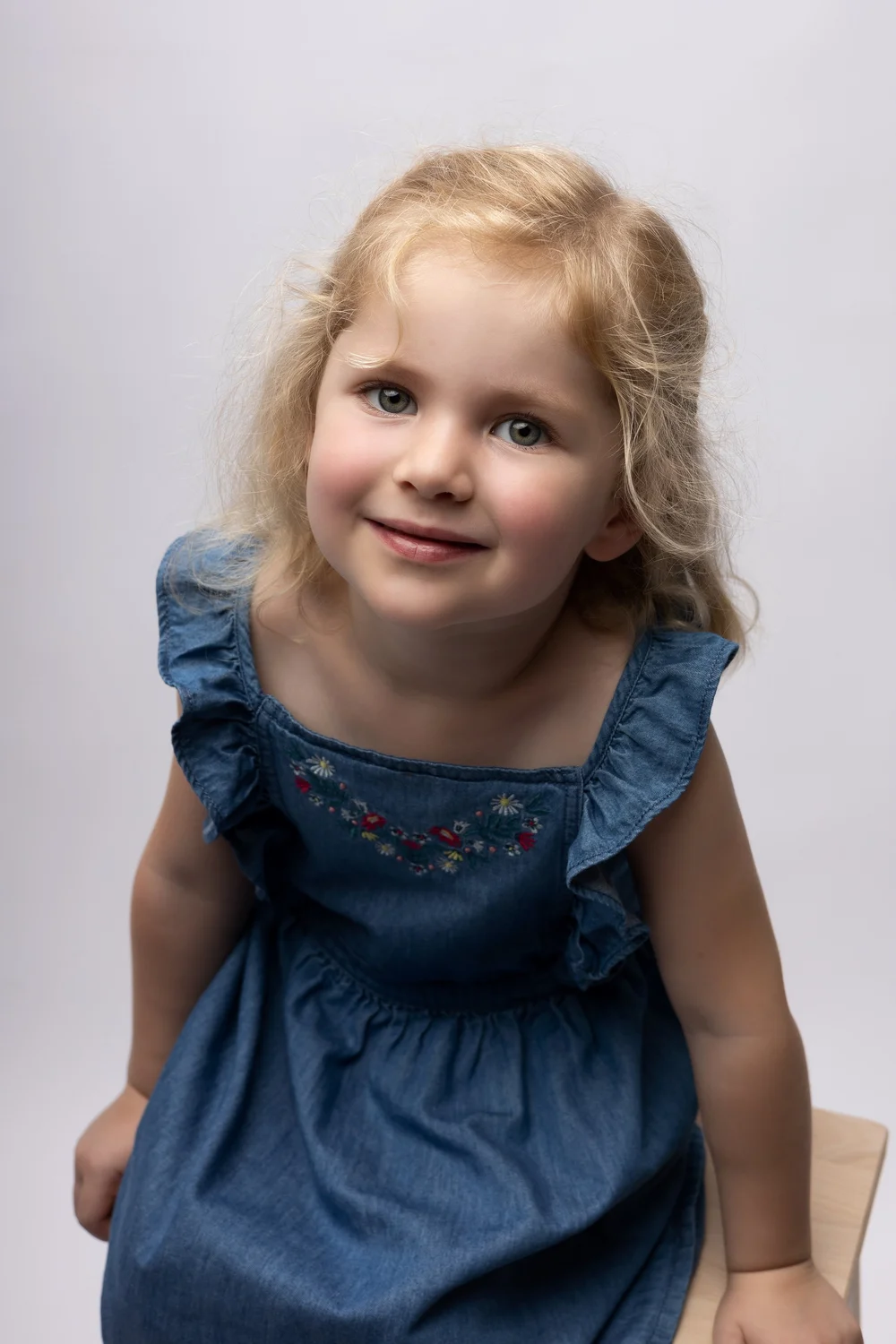 Petite fille en robe en jean, sur fond clair.