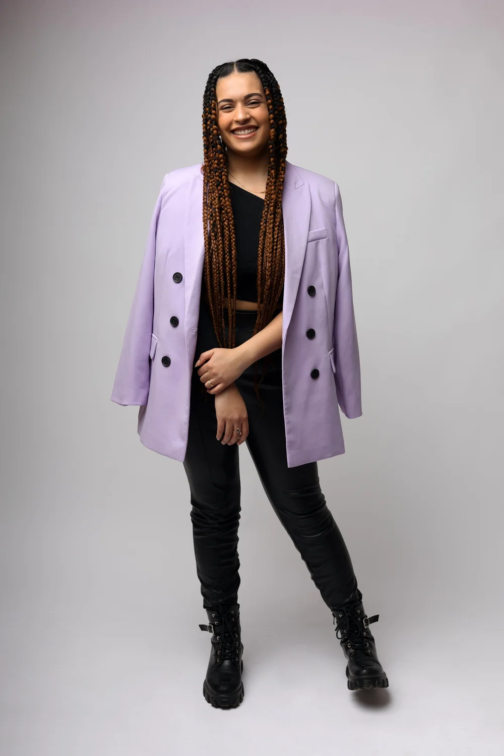 Femme en veste lilas et bottes noires, sur fond clair.