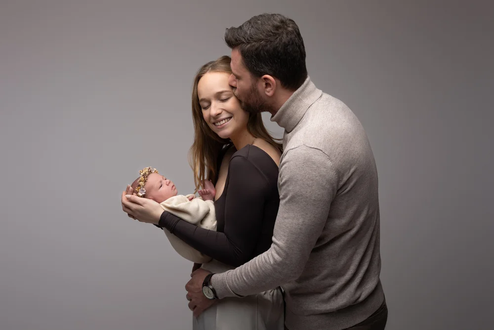 Parents en studio sur fond gris, le nouveau-né dans les bras.