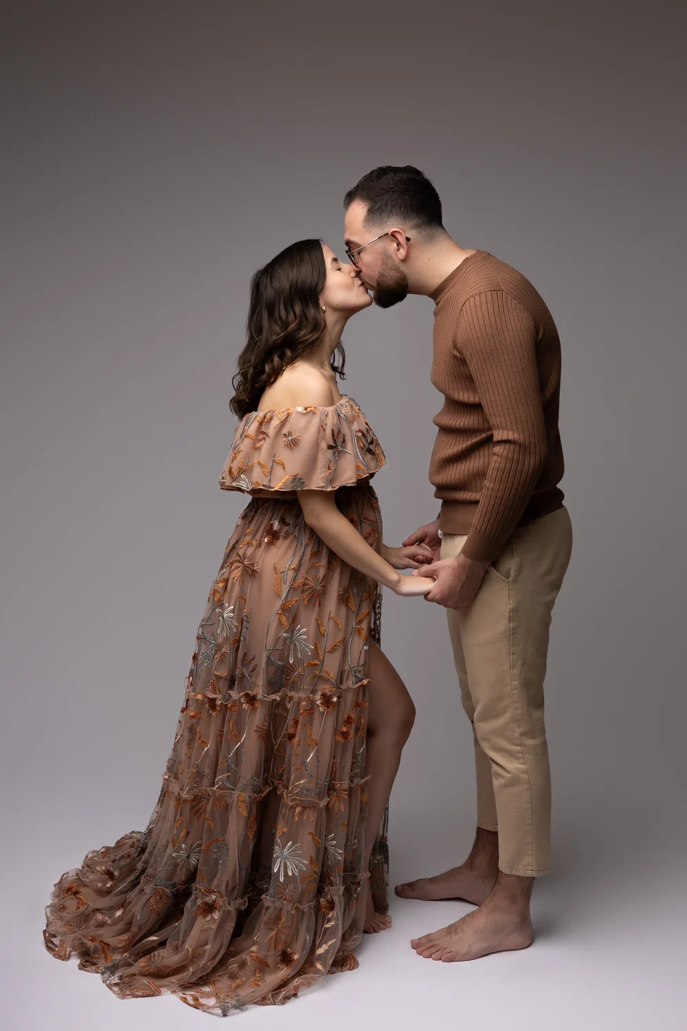 Couple s’embrassant en studio, la femme enceinte en robe fleurie.