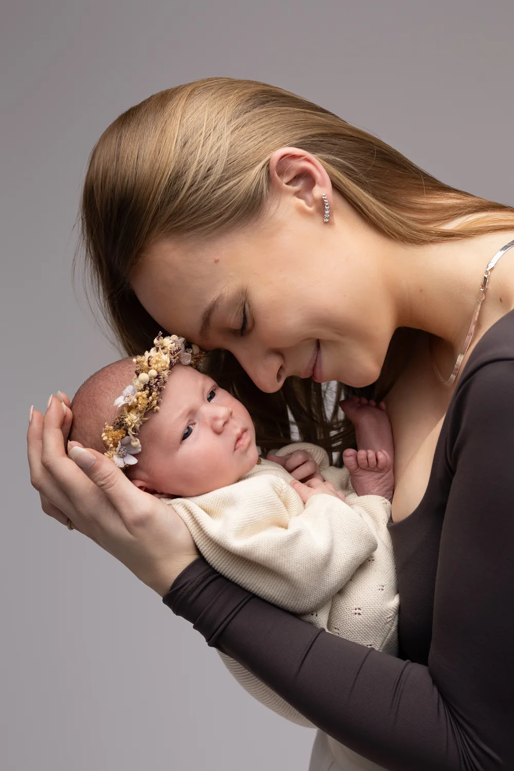 Maman souriante tenant son nouveau-né couronné de fleurs.