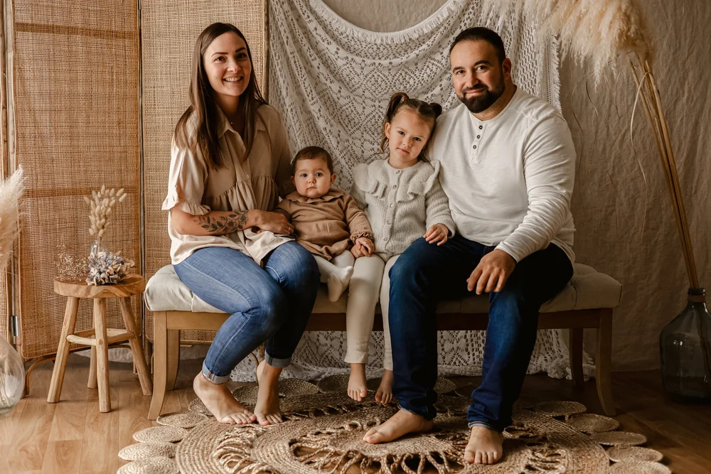 Famille de quatre assise en studio devant un paravent en rotin.