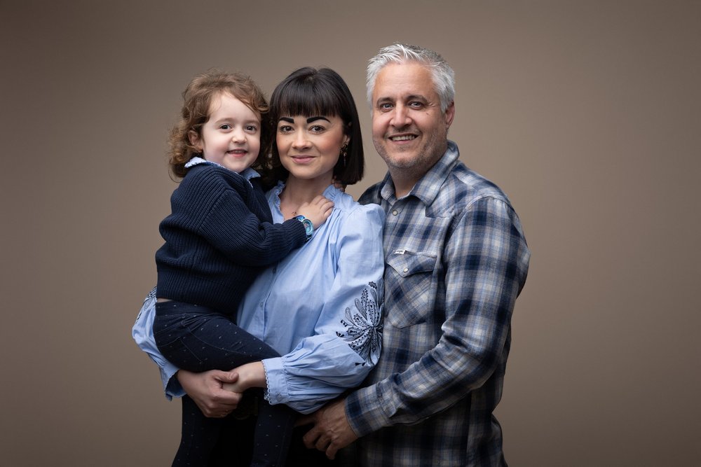 Famille de trois en studio, sur fond gris.