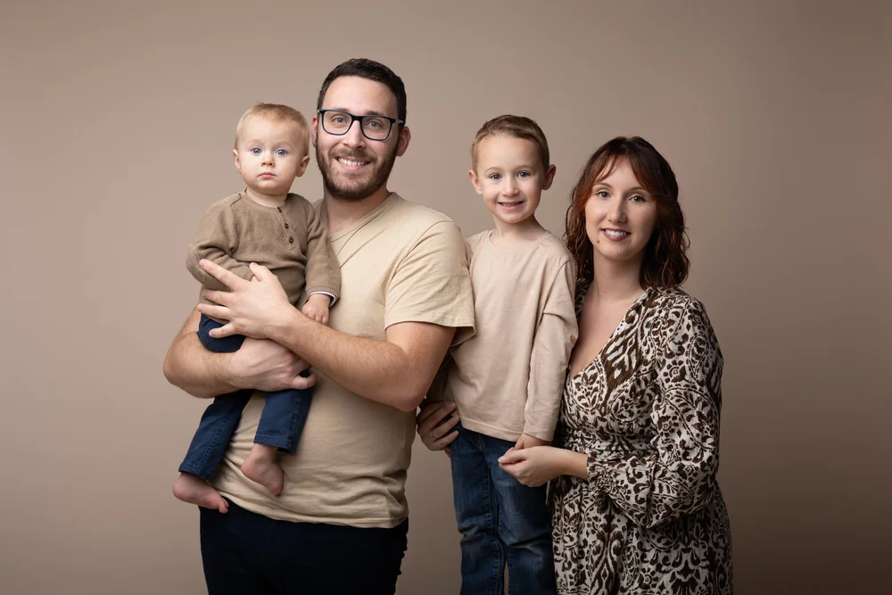 Parents et leurs deux jeunes garçons en portrait de famille, en studio sur fond beige.