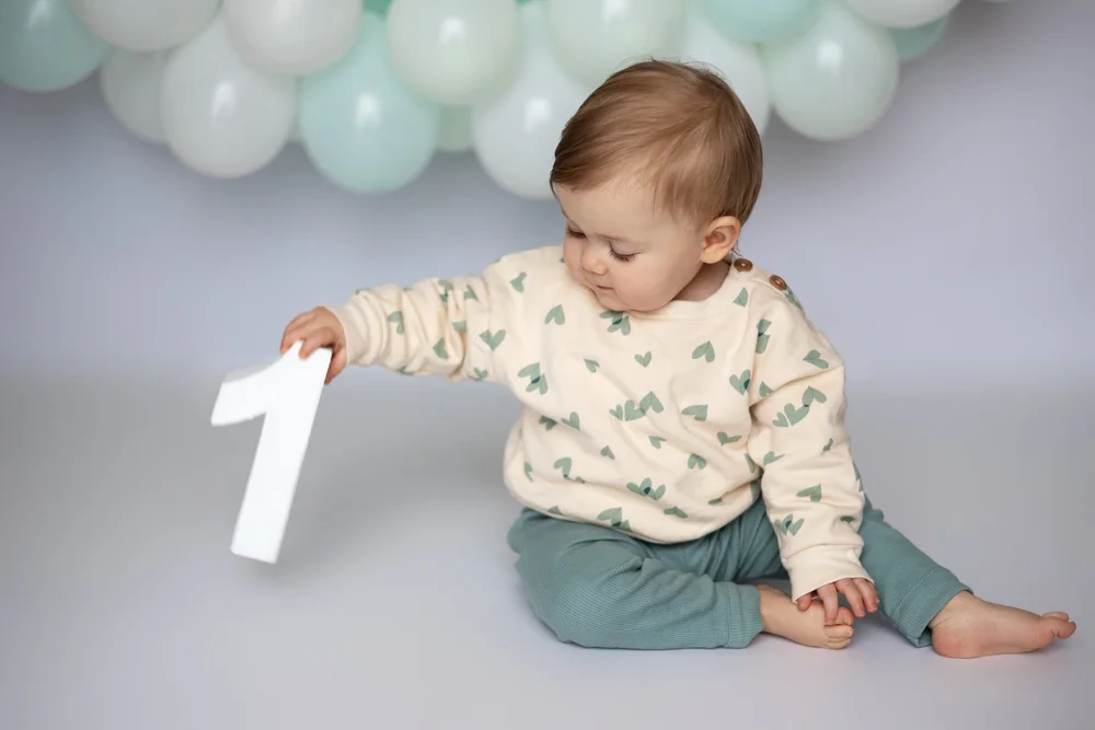 Bébé tenant un chiffre 1 devant des ballons vert d’eau.