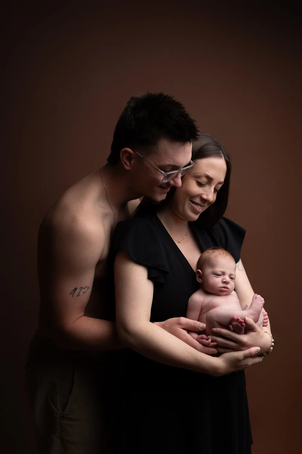 Parents en studio sur fond brun tenant leur nouveau-né.