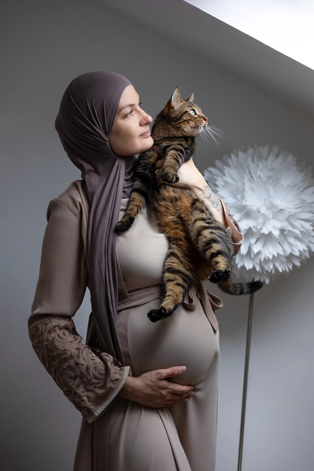 Femme enceinte voilée tenant un chat, près d’une fenêtre.