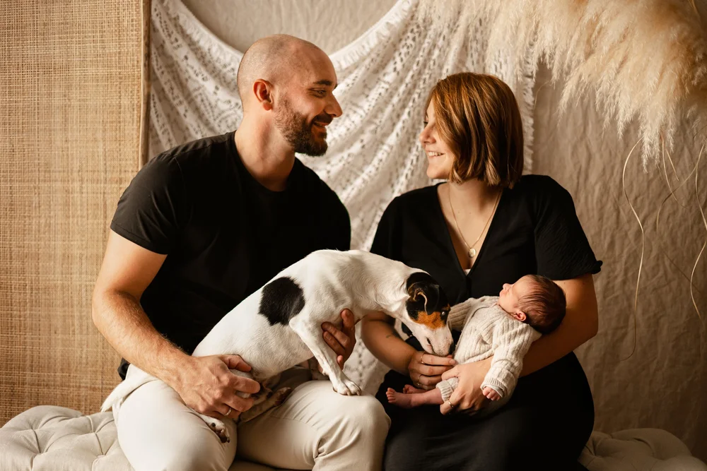 Parents assis en studio avec leur nouveau-né et leur chien.