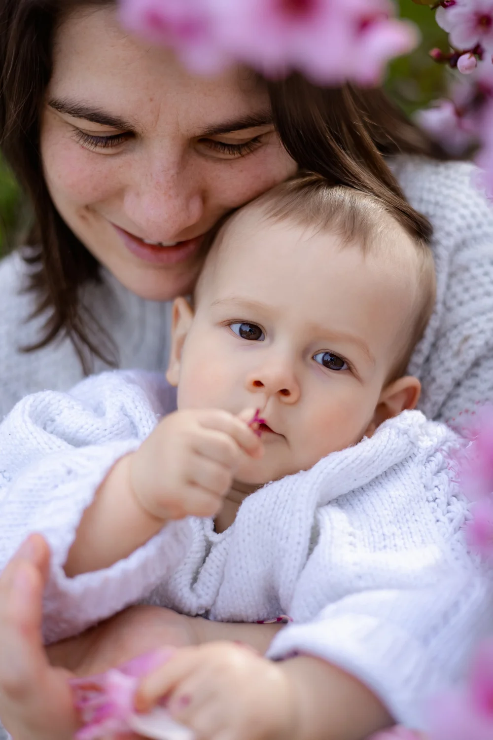 Gros plan d’un bébé contre la joue de sa maman, entre des fleurs roses.