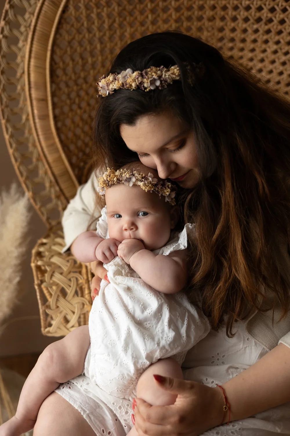 Maman avec une couronne de fleurs tenant son bébé dans un fauteuil en rotin.