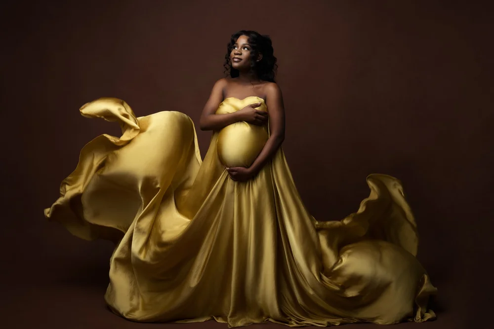 Femme enceinte drapée d’un voile doré qui vole, en studio.
