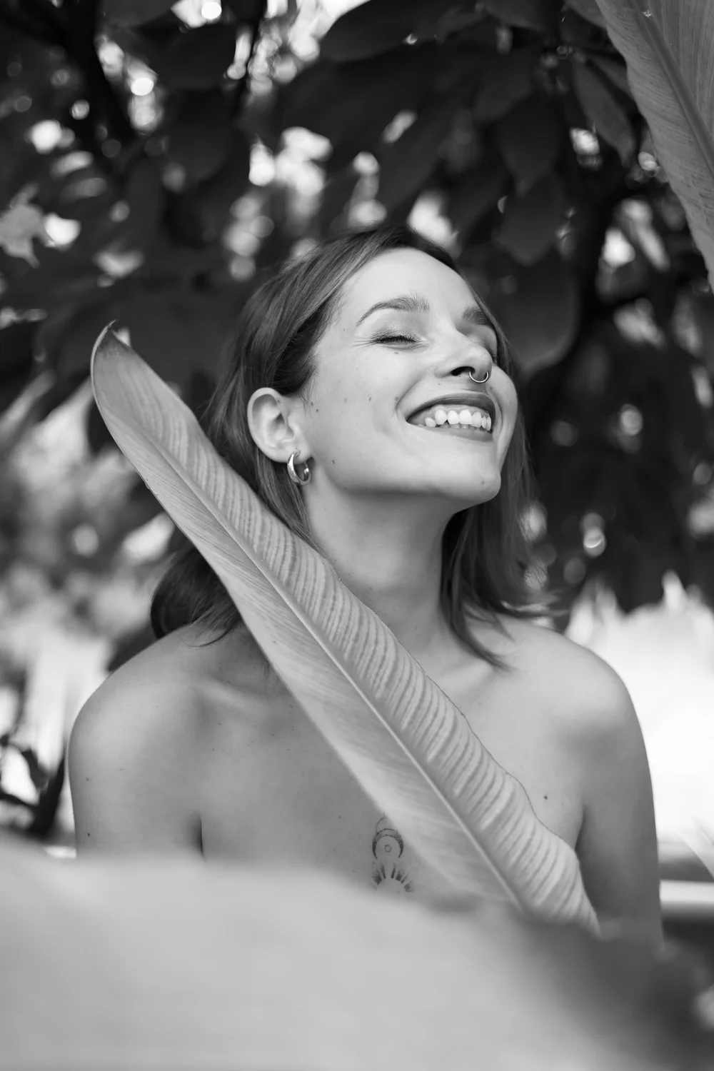 Portrait d’une femme souriante avec une feuille, en noir et blanc.