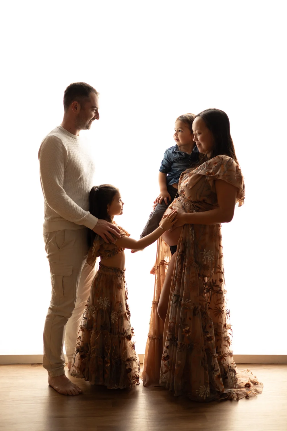 Famille avec deux enfants en contre-jour, la maman enceinte en robe fleurie.