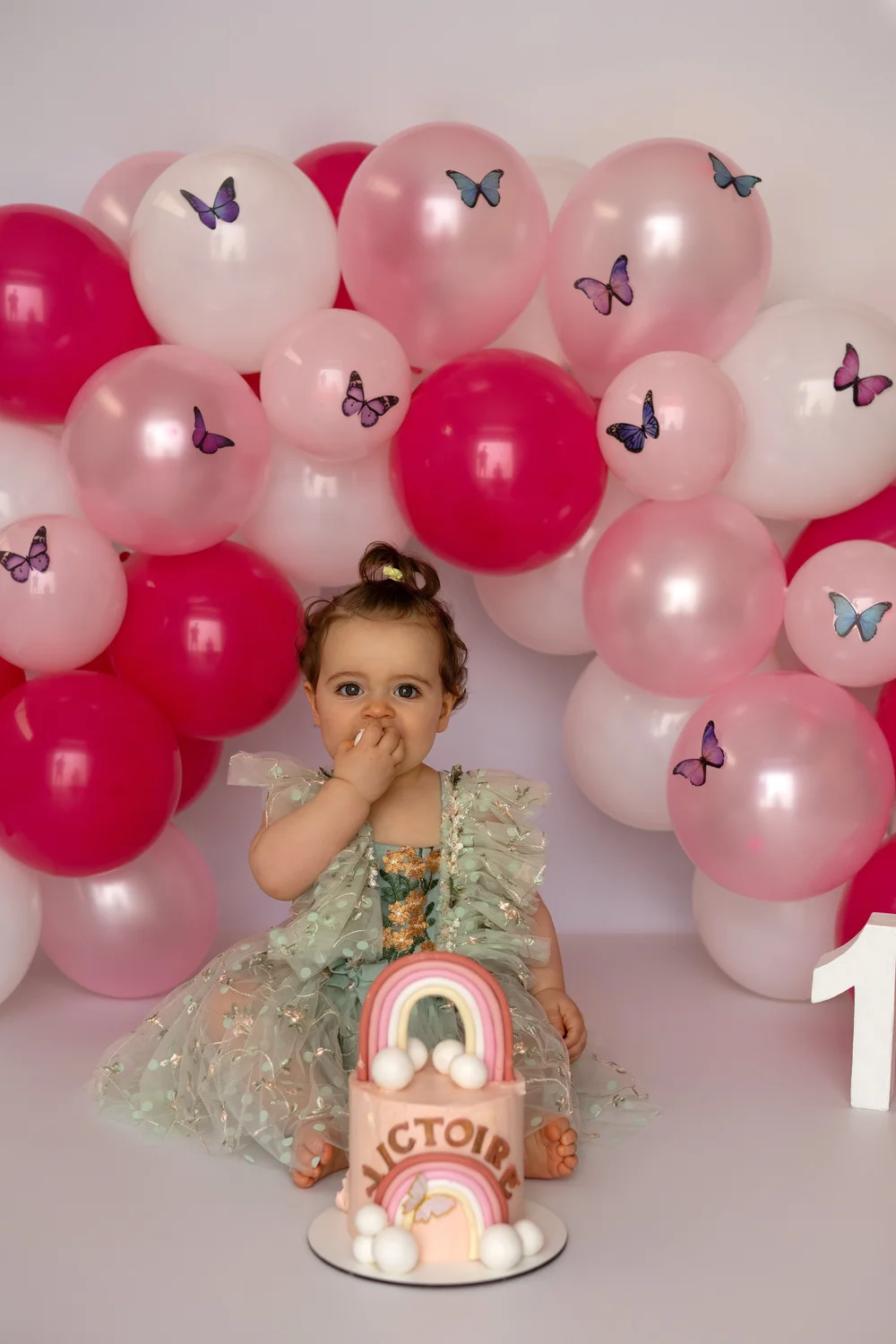 Petite fille devant une arche de ballons roses et fuchsia avec son gâteau.