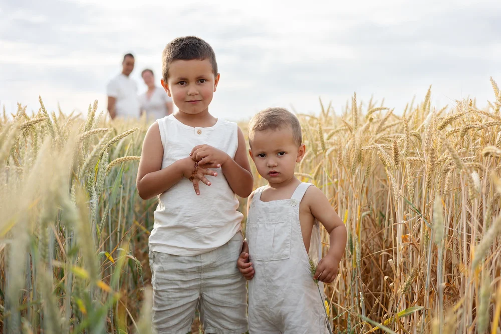 Deux frères dans un champ de blé, leurs parents derrière eux.