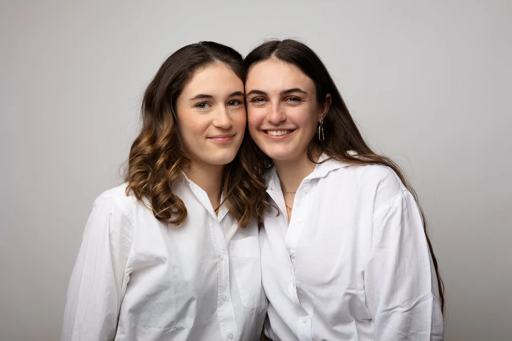 Deux sœurs en chemise blanche, sur fond gris.
