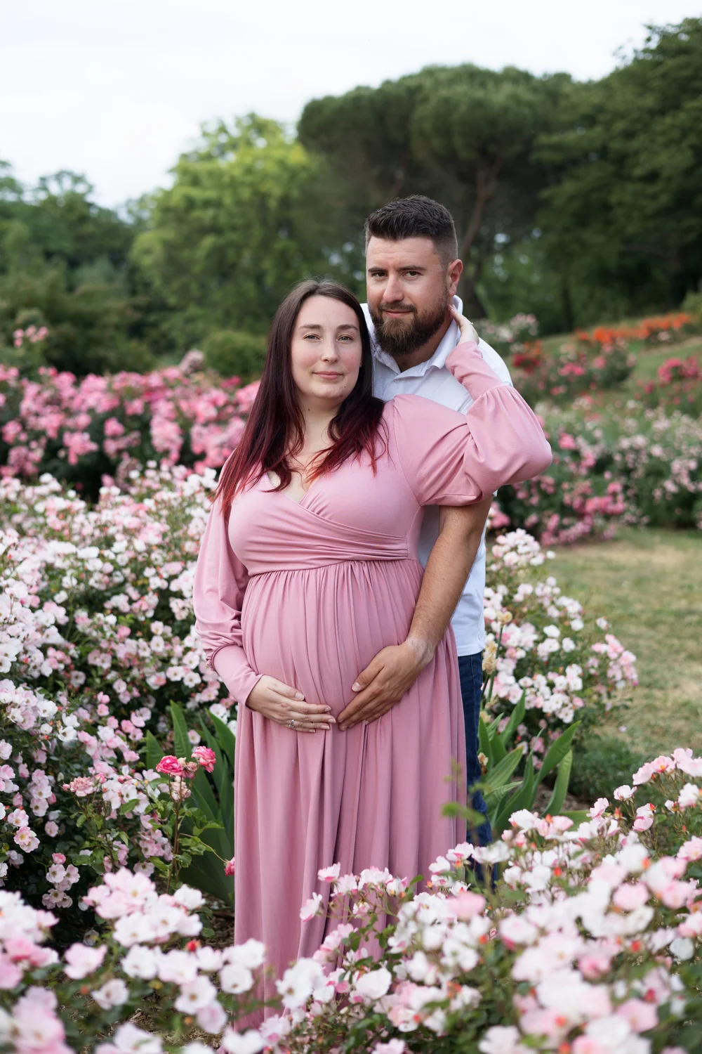Couple dans un jardin de roses, la femme enceinte en robe rose.