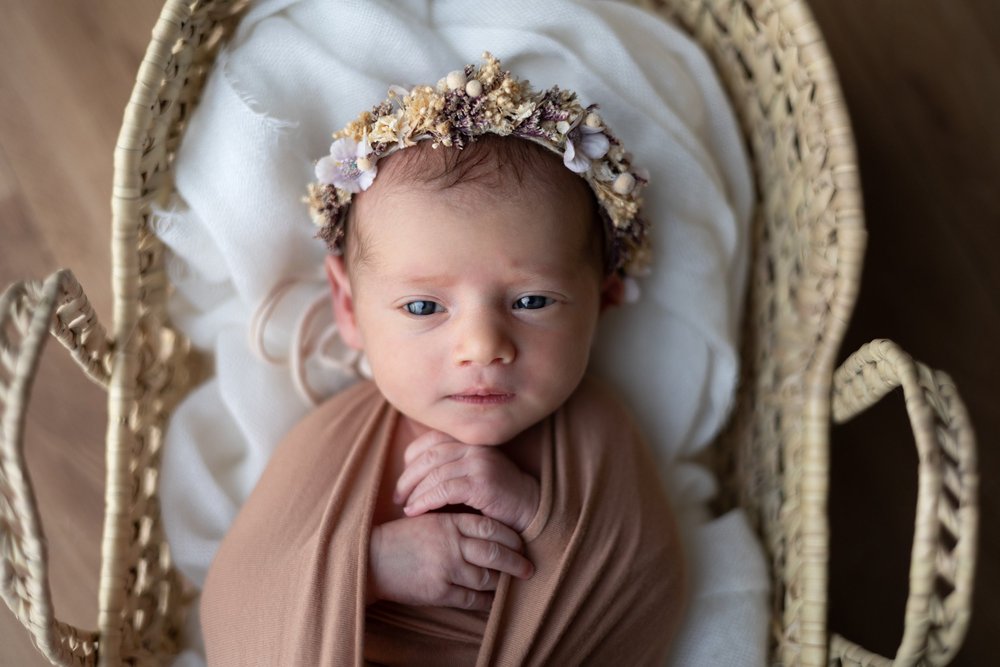 Nouveau-né emmailloté de rose, couronne de fleurs, dans un couffin.