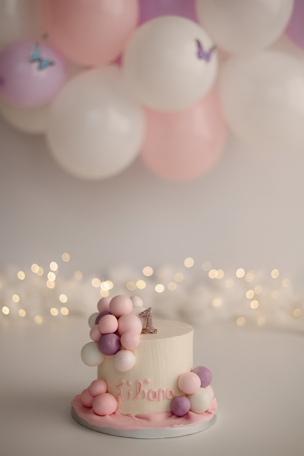Gâteau d’anniversaire rose décoré de boules, devant des ballons pastel.