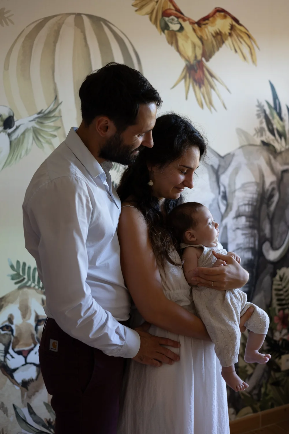 Parents tenant leur nouveau-né devant un papier peint d’animaux.