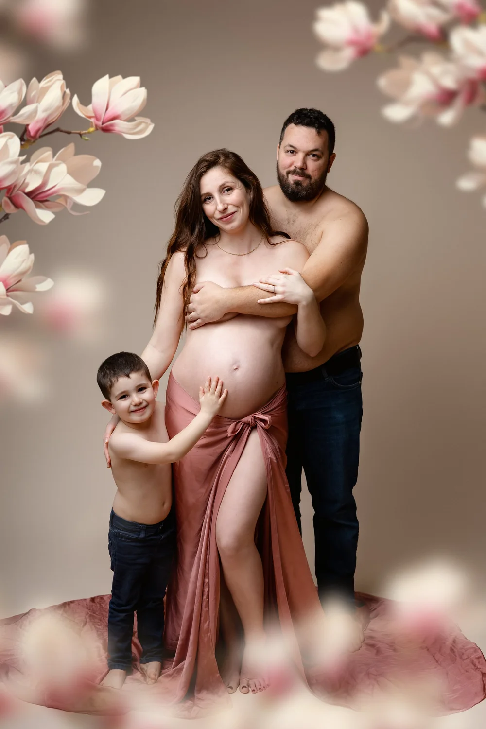 Futurs parents et leur fils posant parmi des branches de magnolia, en studio.