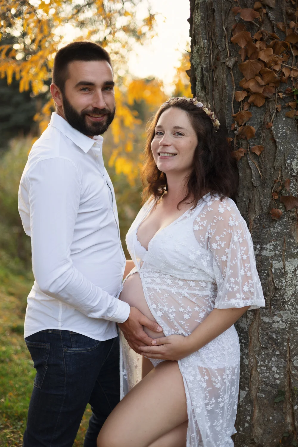 Couple sous un arbre en automne, la femme enceinte en robe blanche.