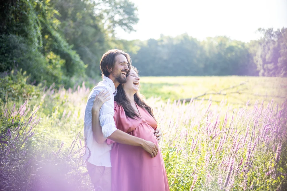 Couple attendant un enfant, enlacé au milieu de fleurs mauves en bord de champ.