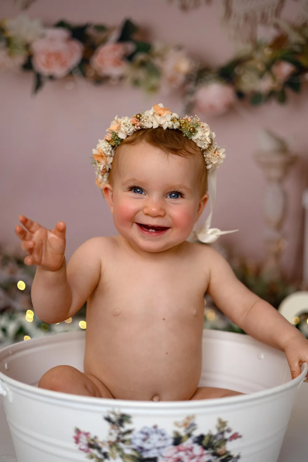 Bébé riant avec une couronne de fleurs dans une bassine fleurie.
