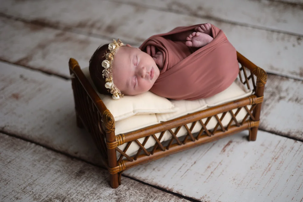 Nouveau-né emmailloté de vieux rose dans un petit lit en rotin.